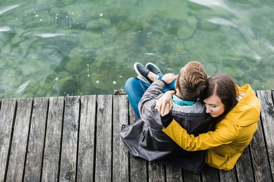Couple in raincoats sitting on the peer of the lake