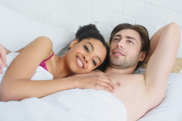 portrait of young smiling interracial couple lying in bed in morning at home