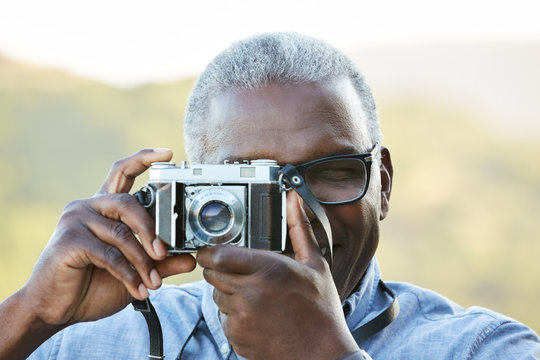 Close up portrait of African American Senior man taking a photo with a vintage film camera outdoors