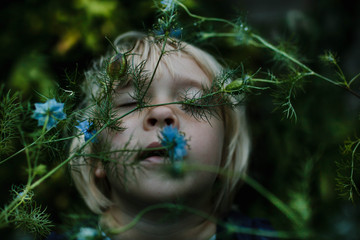 Young girl puts her face against Nigella flowers at dusk.