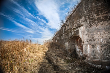 old destroyed wall with deepening in the field of dried grass and blue sky with clouds