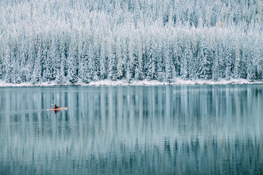 Kayaker floating in a red boat on a beautiful calm lake with fresh snow in the winter