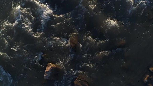 Aerial drone scene of barrancas river at sunset, golden hour at windy day, backlight with flare. The river divides the state of Neuquen from Mendoza in Argentina. Top view, cenital, of water and rocks