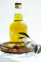 bottle with aromatic oil with green olives on wooden board with branch on white table