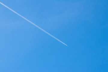 background. The plane flies high in the blue sky, leaving behind a white trace