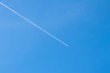 background. The plane flies high in the blue sky, leaving behind a white trace