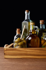 different bottles of aromatic olive oil and jar with green olives on wooden table on black background