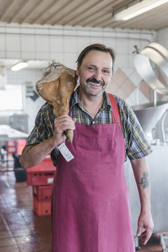 Senior artisan butcher man smiling with cured pig leg over his s