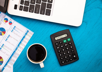 Investment, finance and work concept with charts and graphs and laptop, coffee, calculator on blue board flat lay