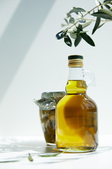 bottle of aromatic olive oil, branch and jar with green olives on table