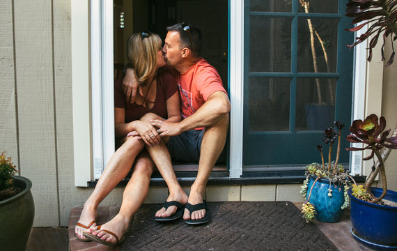 Married middle aged couple sitting in the doorway kissing
