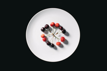 top view of ripe red and yellow sweet cherries on round white plate isolated on black