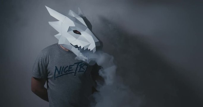 Male wearing dragon head low poly paper craft mask exhaling smoke from a vapor. 4K UHD 60 FPS SLOW MOTION
