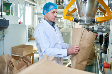 Side view portrait of senior factory worker filling paper bags in packaging section of modern food factory, copy space