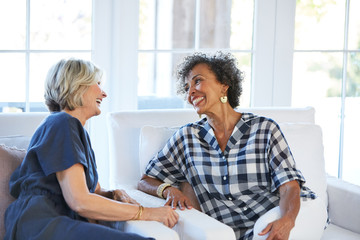 Senior women friends visiting and talking in the living room at home