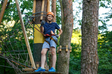 Naklejka na ściany i meble Happy, cute, young boy in blue t shirt and helmet having fun and playing at adventure park, holding ropes and climbing wooden stairs. active lifestyle concept