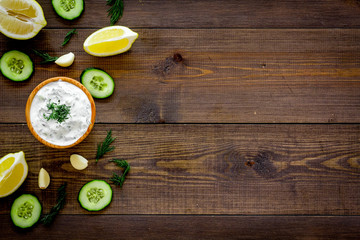 Obraz na płótnie Canvas Greek yogurt dip with greenery, cucumber, oranges, garlic on dark wooden background top view space for text pattern, frame