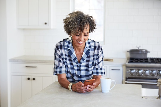 Senior African American Woman Texting On Mobile Phone In Kitchen