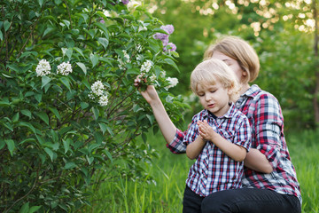 Mother and son in plaid shirts. Woman and boy are standing by flowering bush of lilac. Family time together.