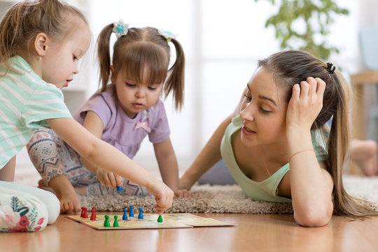 Happy family. Young mother playing ludo boardgame with her children daughters while spending time together at home.