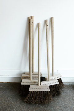 small wooden brooms leaning against white wall in curated shop