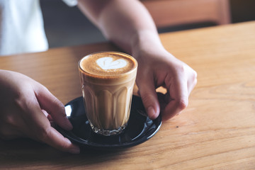 Closeup image of woman's hands holding and giving a glass of hot coffee with heart latte art on...