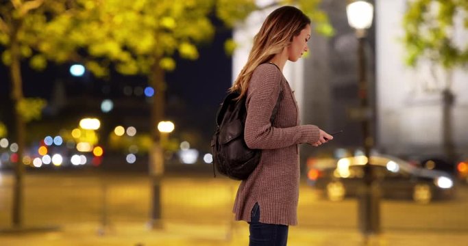 Caucasian woman in the city using her smartphone smiling, Millennial female texting on her mobile phone at night, 4k