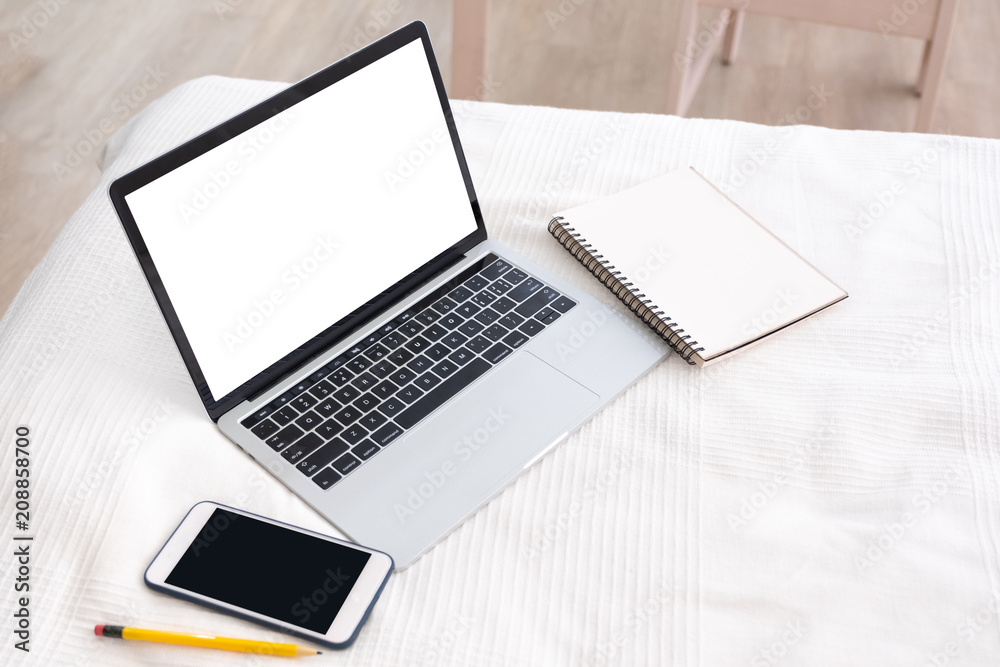 Poster Mock up white screen of laptop with mobile phone and blank notebook on bed blanket in bedroom.working at  home concept.copy space for adding design or text with clipping path.