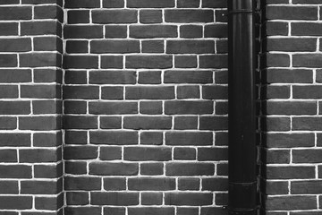 Black brick wall with black downspout. Drain pipe is in right. Bright geometric and symmetrical background image of monochrome brick wall.