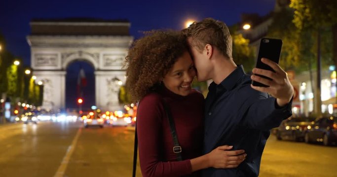 Happy and attractive couple take a selfie on Paris street at night, Caucasian male and female take a picture together near the Arc de Triomphe in evening, 4k