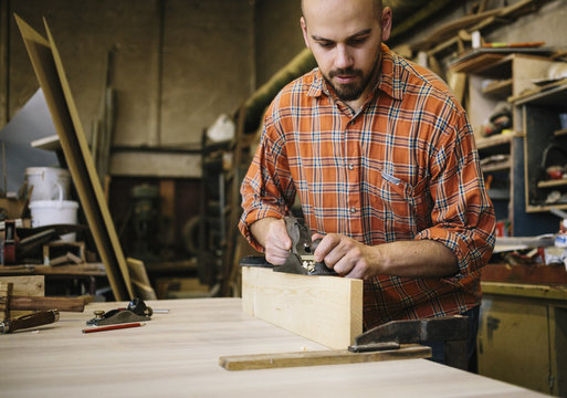 Carpenter working with smoothing bench plane in his workshop