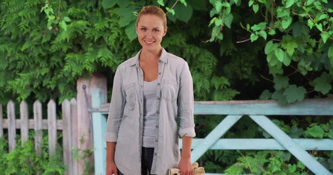 Good-looking Caucasian woman out gardening posing cheerfully by wooden fence, Young woman standing outside looking at camera with happy expression on face, 4k