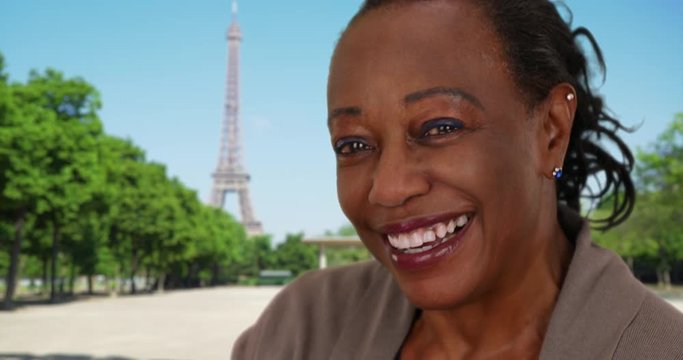 Cute mature black woman in Paris smiling and laughing at camera, Portrait of retired African American female standing near Eiffel Tower, 4k