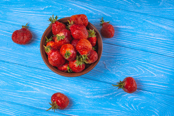 Strawberries in a bowl on a blue wooden surface