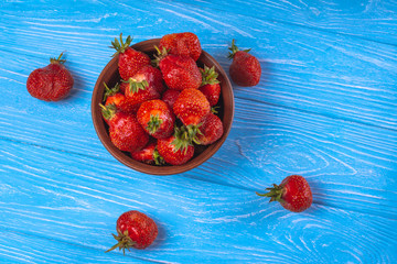 Strawberries in a bowl on a blue wooden surface - Powered by Adobe