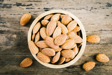 Almonds in brown bowl on textured wooden background.