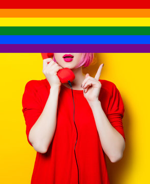 portrait of beautiful surprised young woman with red handset on the wonderful yellow studio background with rainbow