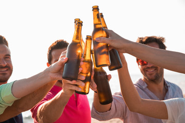 Cheers! Group of happy young people are toasting with bottles of beer in the beach. Celebration...