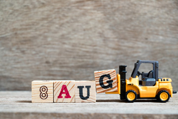 Toy forklift hold block G to complete word 8 aug on wood background (Concept for calendar date in month August)