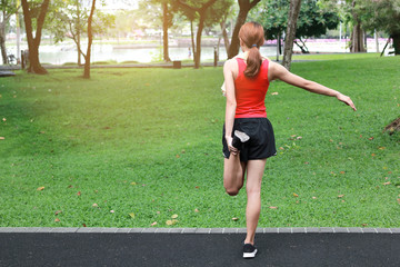 Back view of healthy Asian woman stretching her legs before run in park. Fitness and exercise concept.