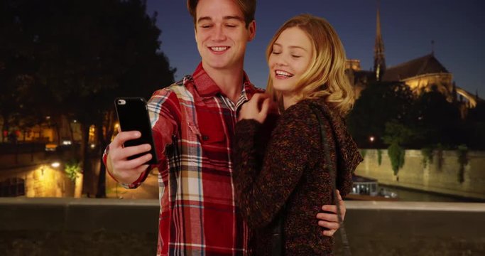 Happy young couple taking fun selfies in Paris at night, Smiling male and female taking picture together to share with friends, 4k