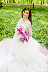 Lovely girl in a white dress sitting on the grass in a park with a bouquet in her hands