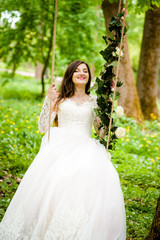 Obraz na płótnie Canvas Beautiful bride is sitting on a swing decorated with flowers in the park