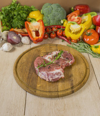 A large piece of steak on a wooden board, against a background of vegetables and greens, a multicolored composition