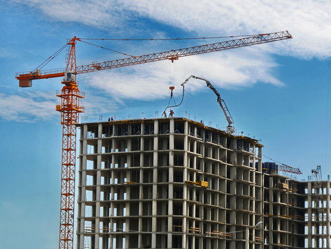Construction crane and concrete building under construction against blue sky. Construction site.