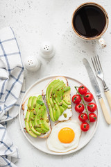 Toast with avocado, fried egg, tomatoes and cup of black coffee americano on bright concrete background. Top view and copy space for text