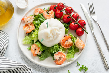 Burrata salad with shrimps, lettuce, tomatoes and olive oil on a white plate. Closeup view. Healthy italian salad