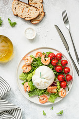 Healthy salad with burrata, shrimps, tomato and lettuce on white plate. Top view of tasty italian salad with olive oil dressing. Healthy eating concept
