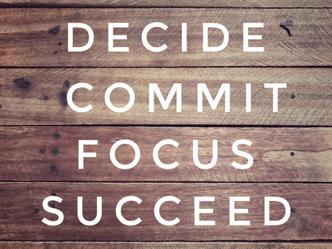 Motivational and inspirational quote - &lsquo; Decide, commit, focus, succeed&rsquo; on a wooden wall. With vintage styled background.