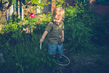 Little toddler boy watering the garden at sunset